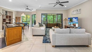 A spacious living area with a kitchen, a dining area, and a balcony with a view of greenery. - Toogoom Beach Vibes. Absolute Beachfront Home with pool! 4BR (Toogoom)