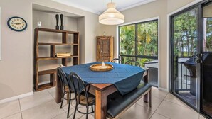 A dining area with a wooden table, chairs, a bench, a hanging light fixture, a clock, and a view of the outdoors through a glass door. - Toogoom Beach Vibes. Absolute Beachfront Home with pool! 4BR (Toogoom)