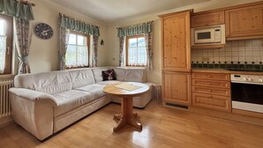 A cozy living room with a beige sofa, a wooden coffee table, and a kitchen area with wooden cabinets and a microwave. - Christoph by Interhome (Haus)