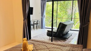 Habitación de hotel con una cama grande, un sofá y un balcón con vistas a zonas verdes.