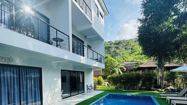 Un edificio moderno de dos pisos con piscina, mobiliario exterior y un césped verde exuberante.