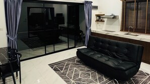 Una sala de estar moderna con un sofá negro, una mesa de comedor con sillas y una zona de cocina con pileta y estufa.