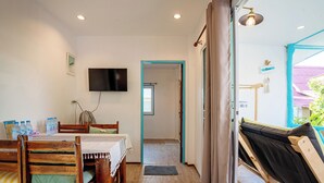 A room with a wooden dining table, chairs, a TV mounted on the wall, a window with curtains, and a bed with a headboard. - Dream Villa Beachfront Sunset (Koh Samui)