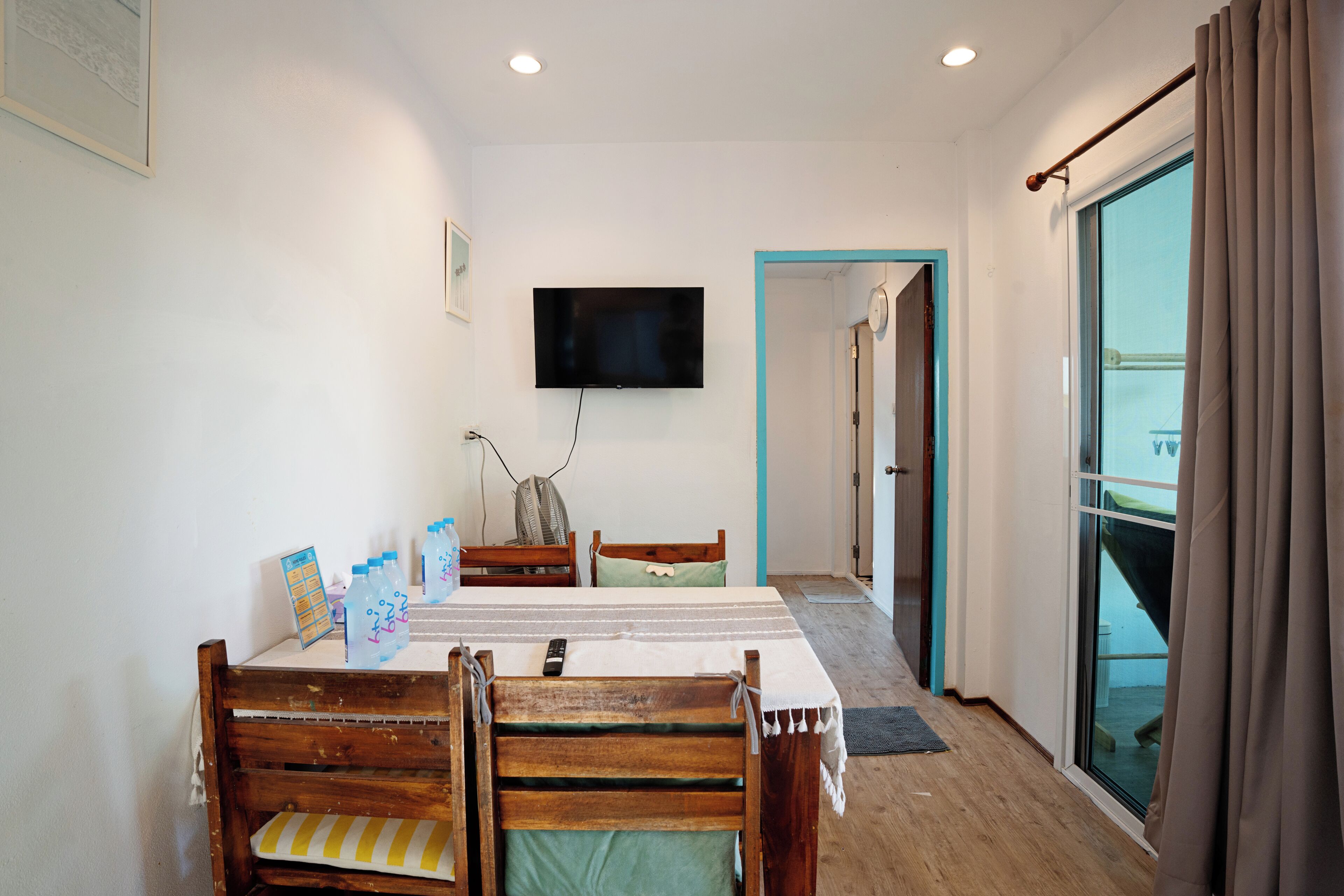 A dining area with a table, chairs, a TV mounted on the wall, and a view through a glass door.
