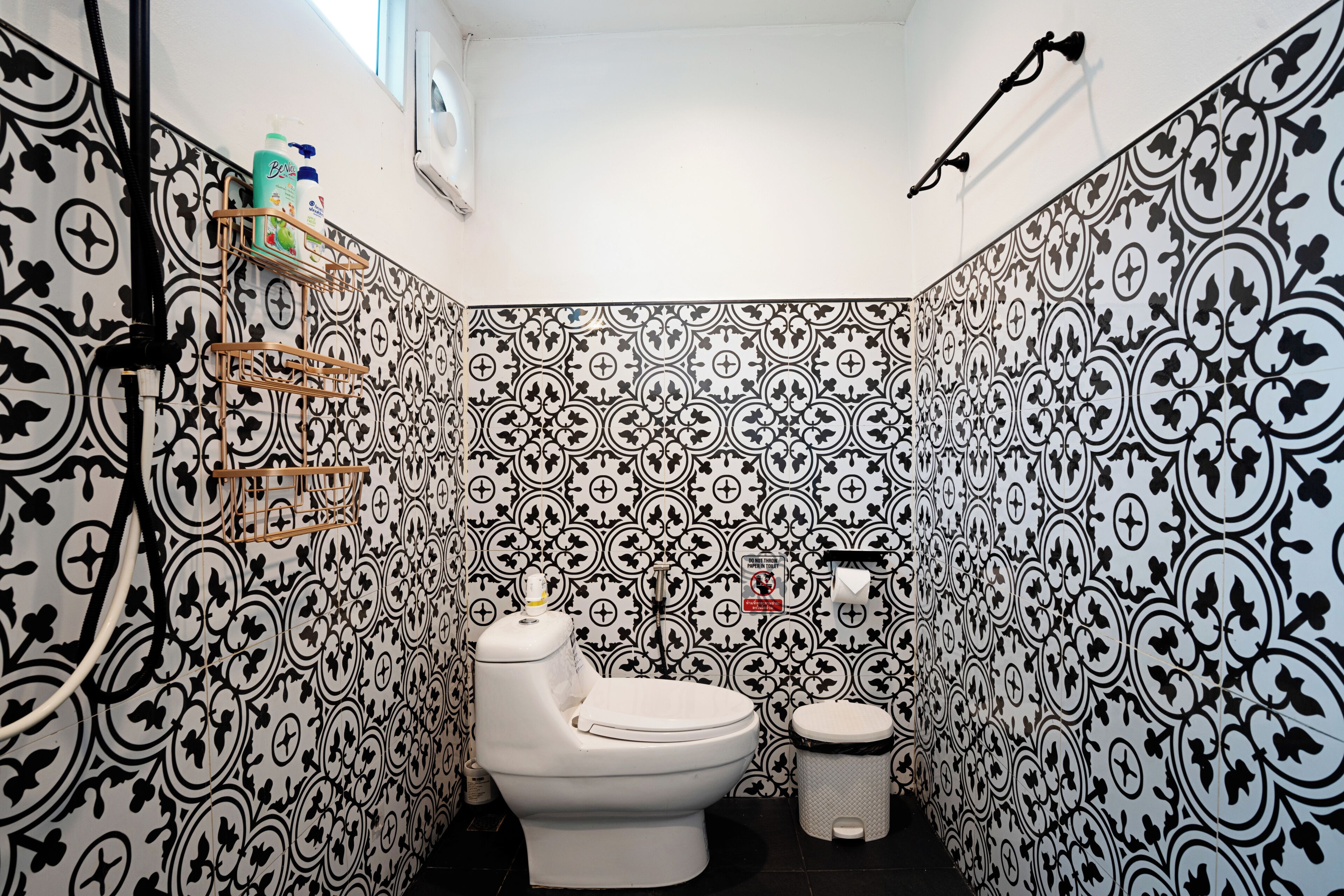 Un baño con pared de azulejos decorativos, inodoro, bidé y estante con artículos de aseo.