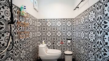 Un baño con pared de azulejos decorativos, inodoro, bidé y estante con artículos de aseo.