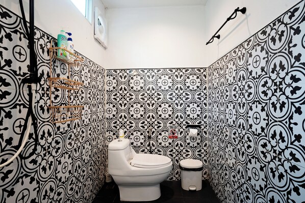 A bathroom with a patterned tile wall, a toilet, a bidet, and a shelf with toiletries. - Dream Villa Beachfront Sunset (Koh Samui)