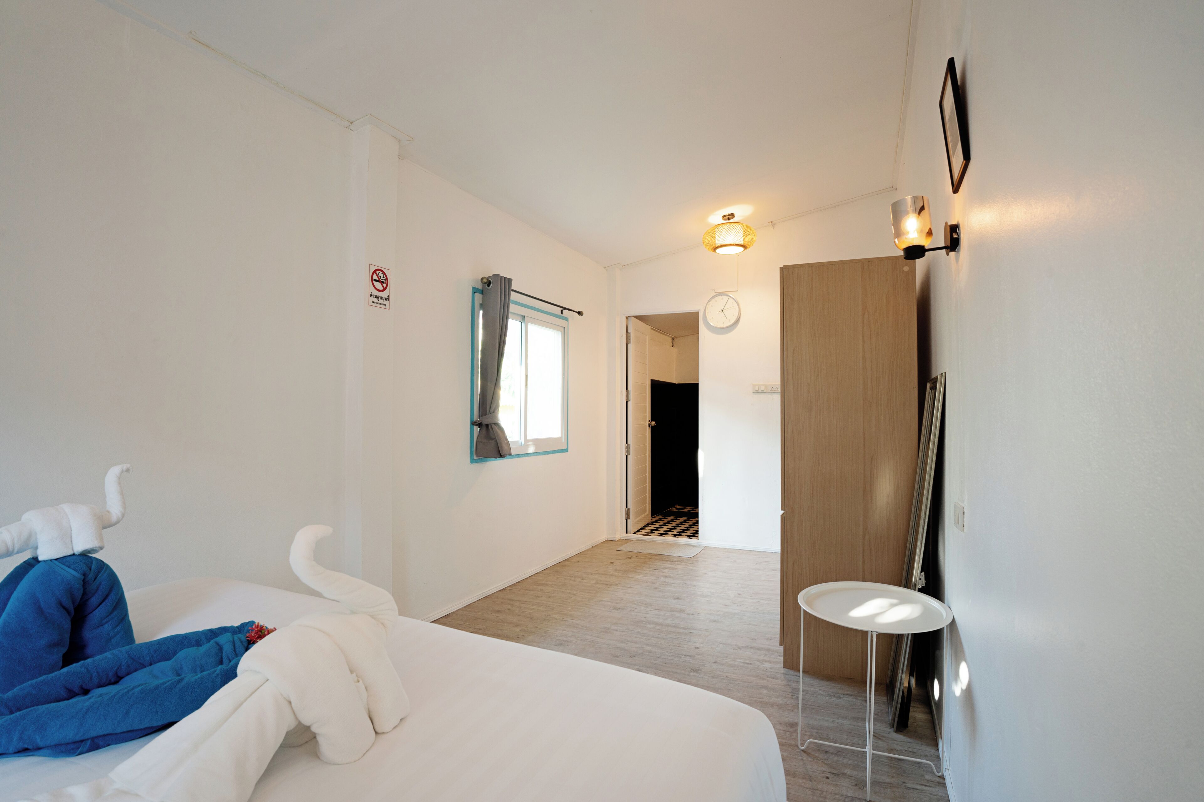 A hotel room with a bed, a small table, a door, and a wall-mounted clock.