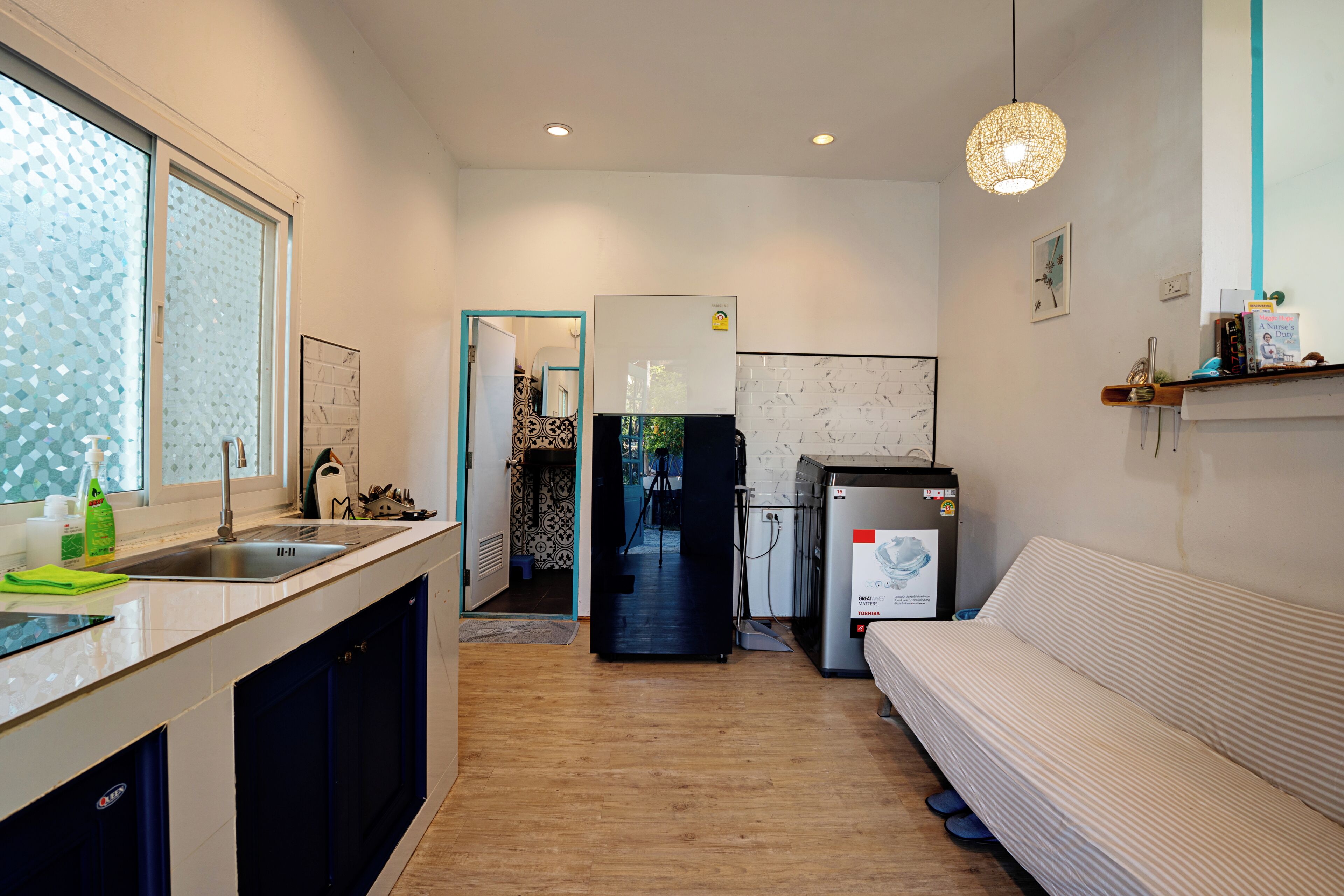 A compact kitchen with a refrigerator, sink, and a sofa in the living area.