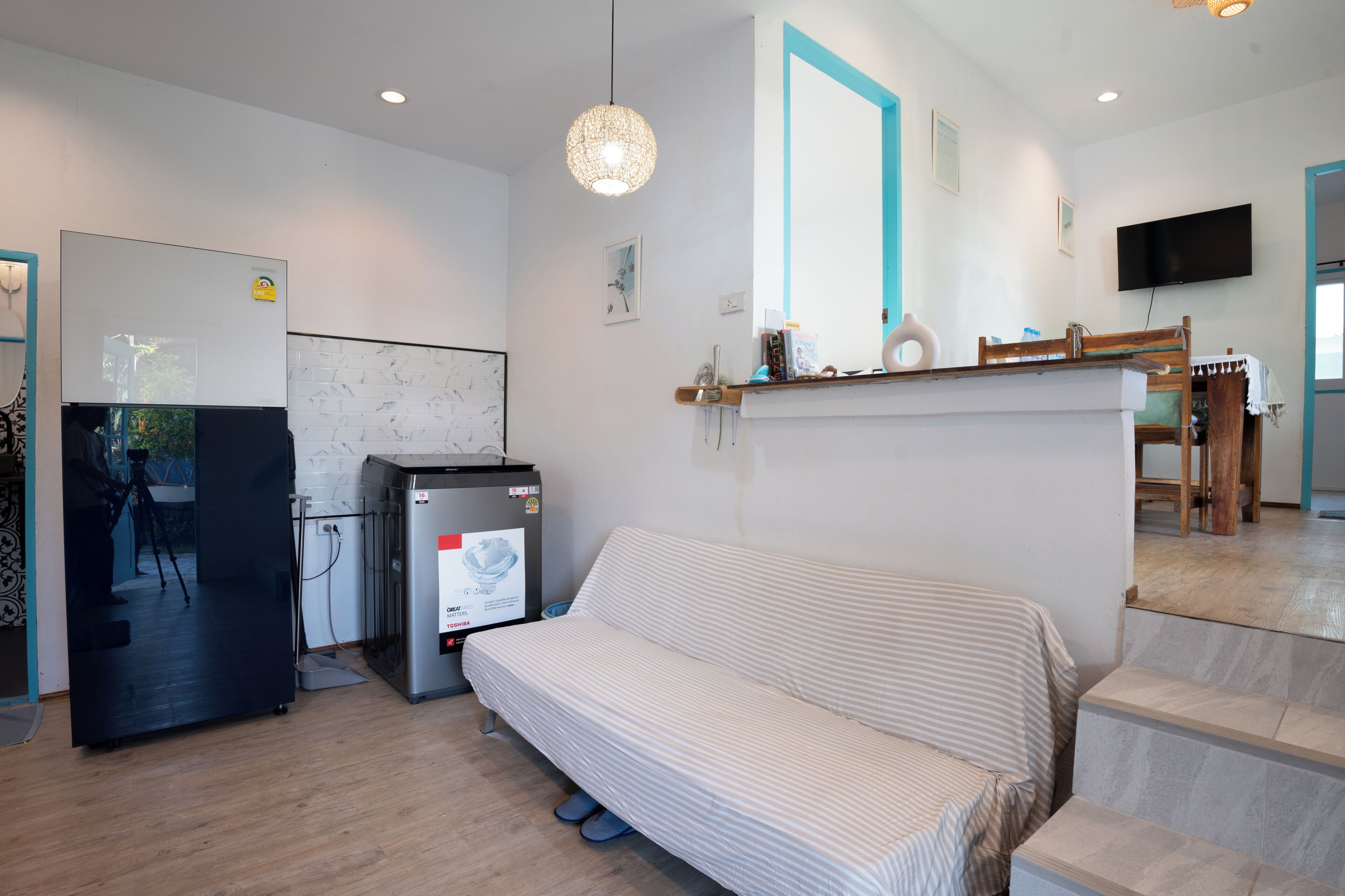 Una cocina moderna con refrigerador, microondas y cafetera. Hay un sofá y un comedor con mesa y sillas.