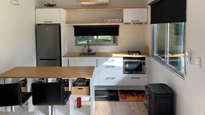 Eine kompakte Küche mit Kühlschrank, Herd und Mikrowelle. Es gibt eine Essecke mit Tisch und Stühlen.