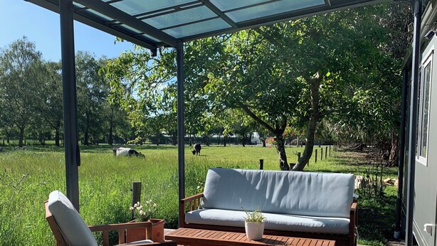 Ein überdachter Außenbereich mit Holzdeck, einer Couch und einem Sessel.