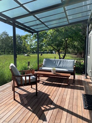 Un espace extérieur aménagé, abrité et doté d’une terrasse en bois, d’un canapé et d’un fauteuil.