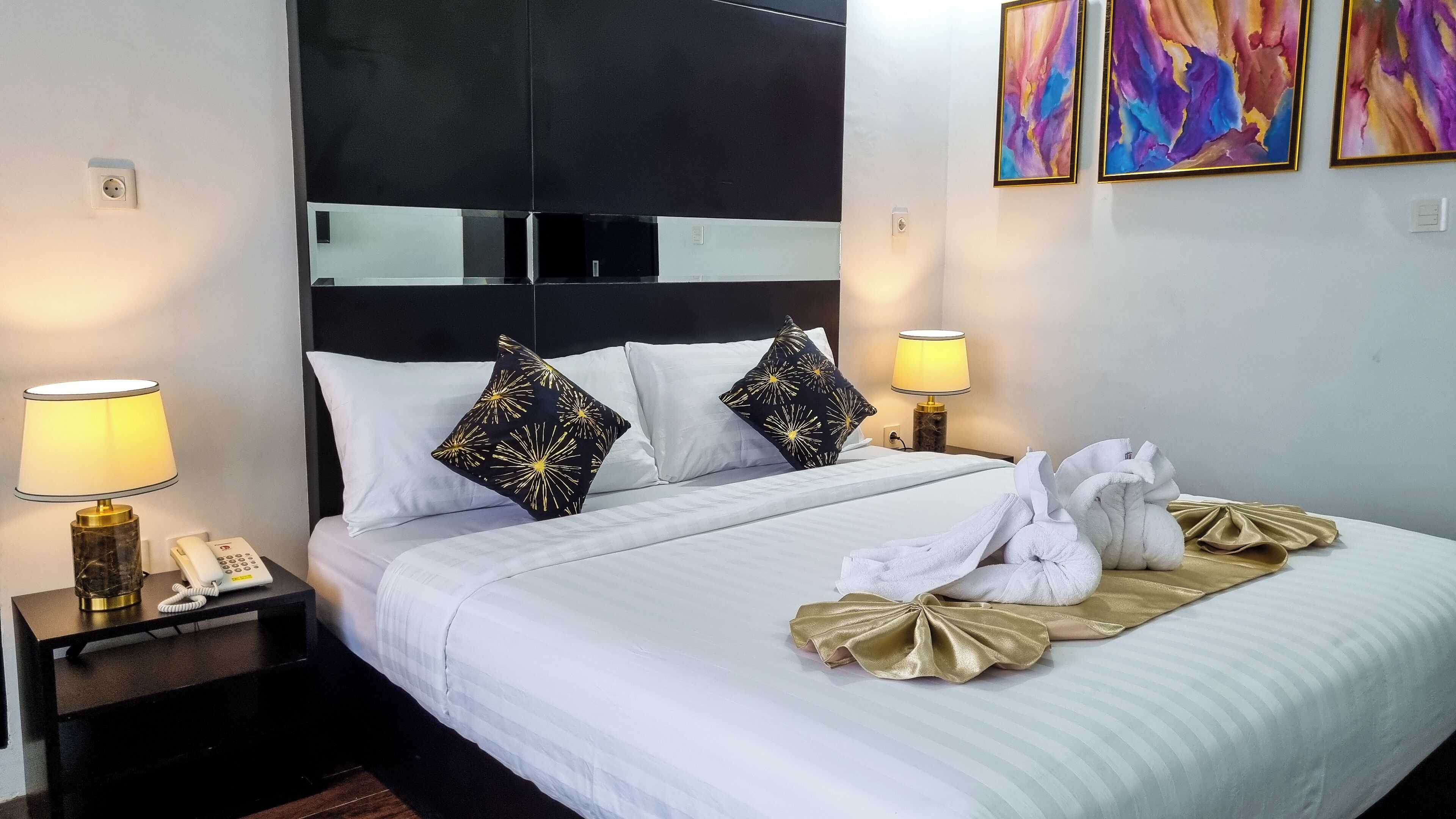 Habitación de hotel con cama, dos lámparas de noche, teléfono y cabecero con espejo.