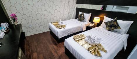A hotel room with two beds, each with white bedding and gold accents, a bedside table with a lamp, and a patterned wall.