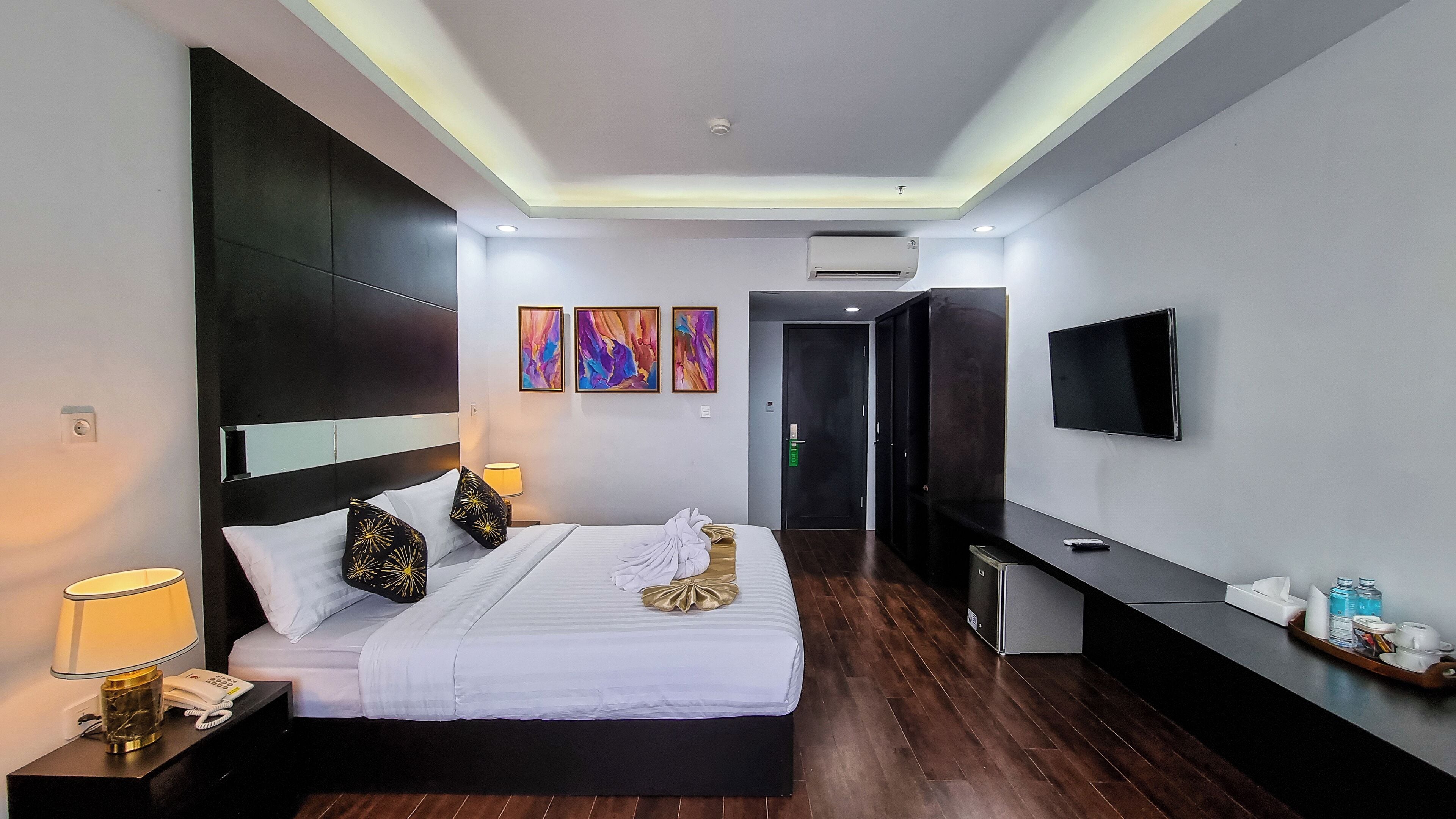Una habitación de hotel moderna con una cama grande, lámparas de noche, un televisor de pantalla plana y obras de arte en las paredes.