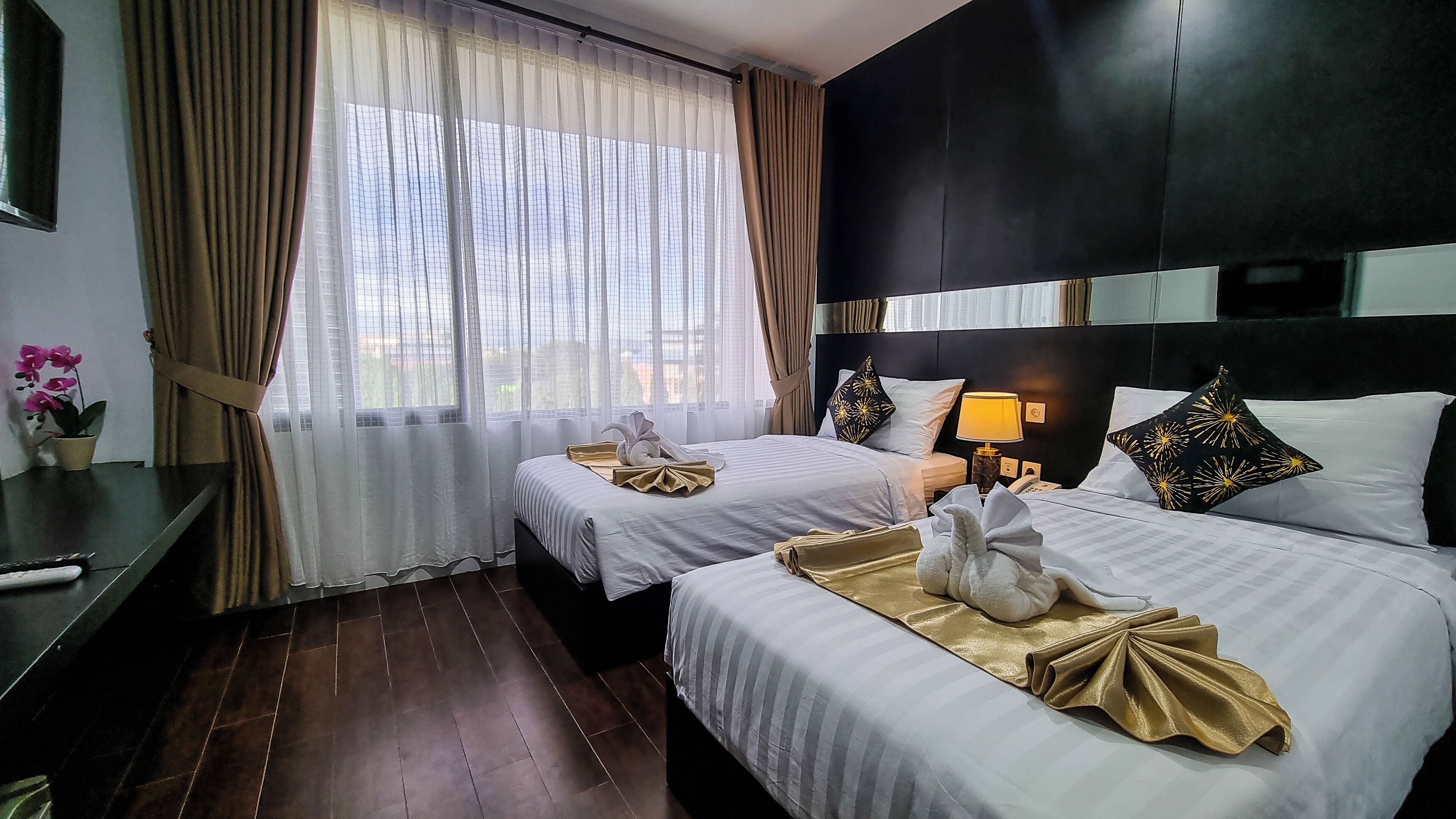 Ein Hotelzimmer mit zwei Betten, einem Schreibtisch, einer Lampe und einem fenster mit Vorhängen.