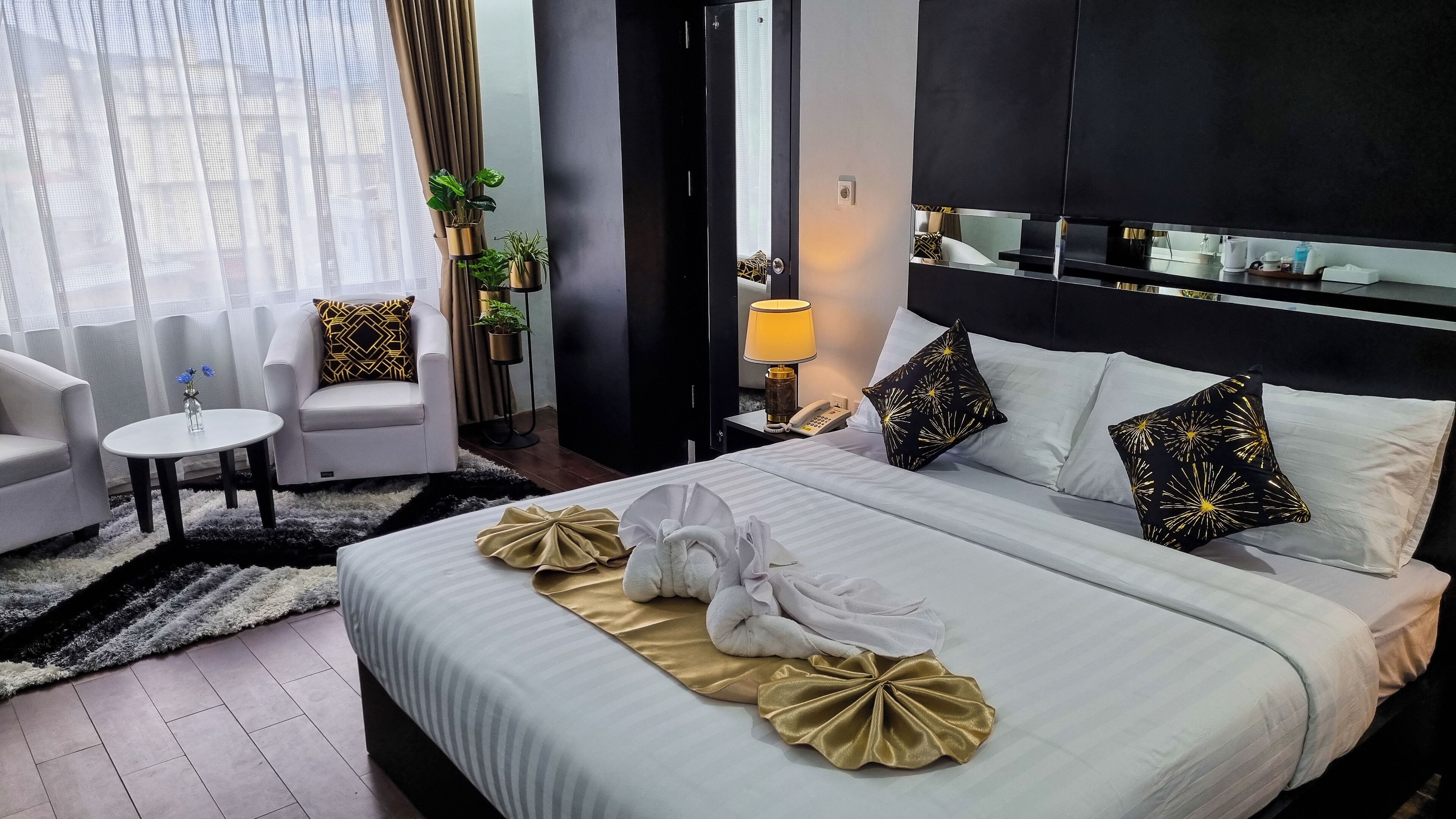 Una camera d'albergo con un letto, un angolo salotto con una sedia e un tavolino, una lampada da comodino e uno specchio a parete.