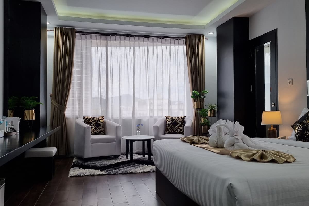 A modern hotel room with a large bed, two armchairs, a small table, and a desk with a lamp.
