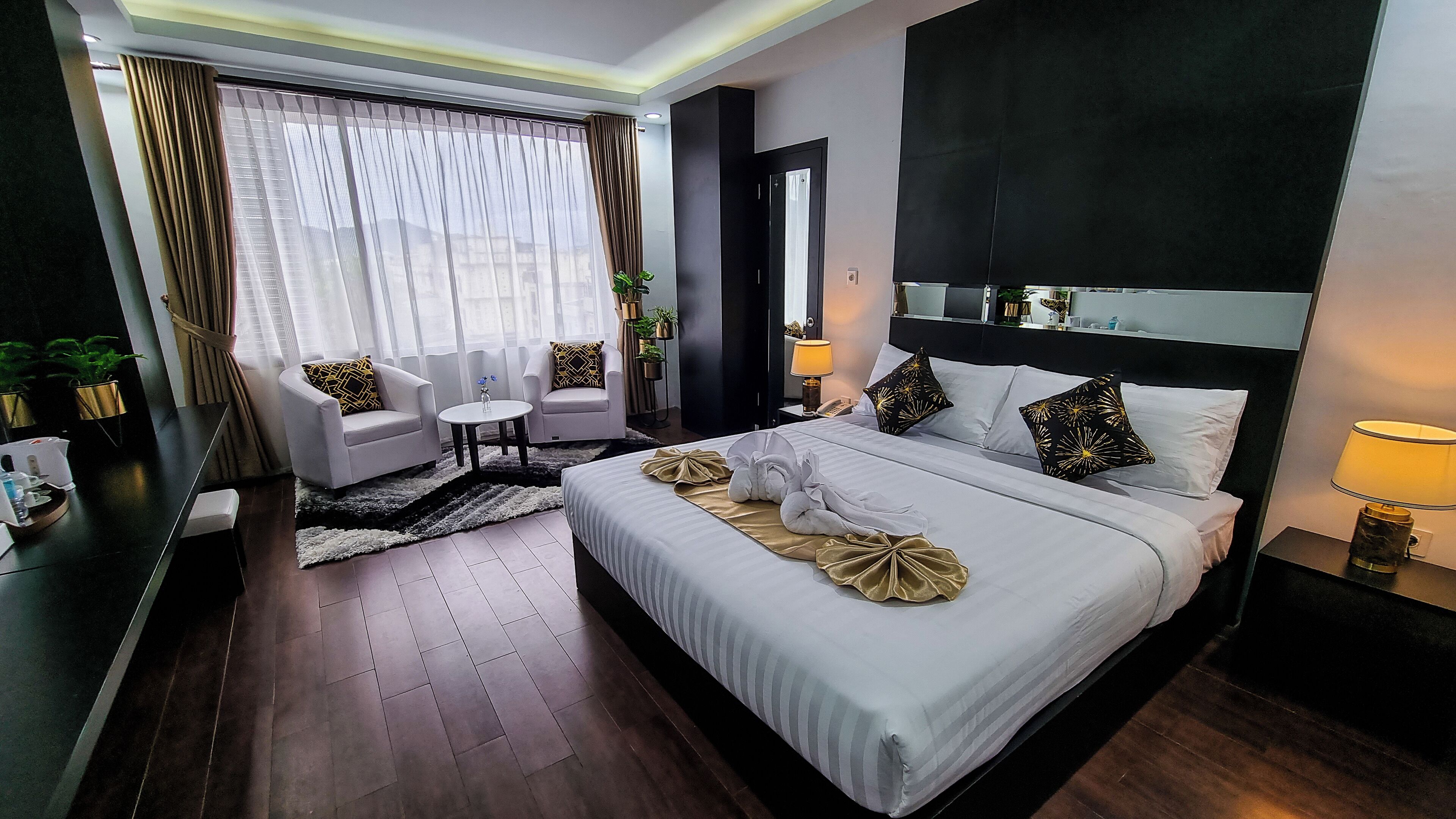 A hotel room with a large bed, two armchairs, a small table, and a desk with a lamp.