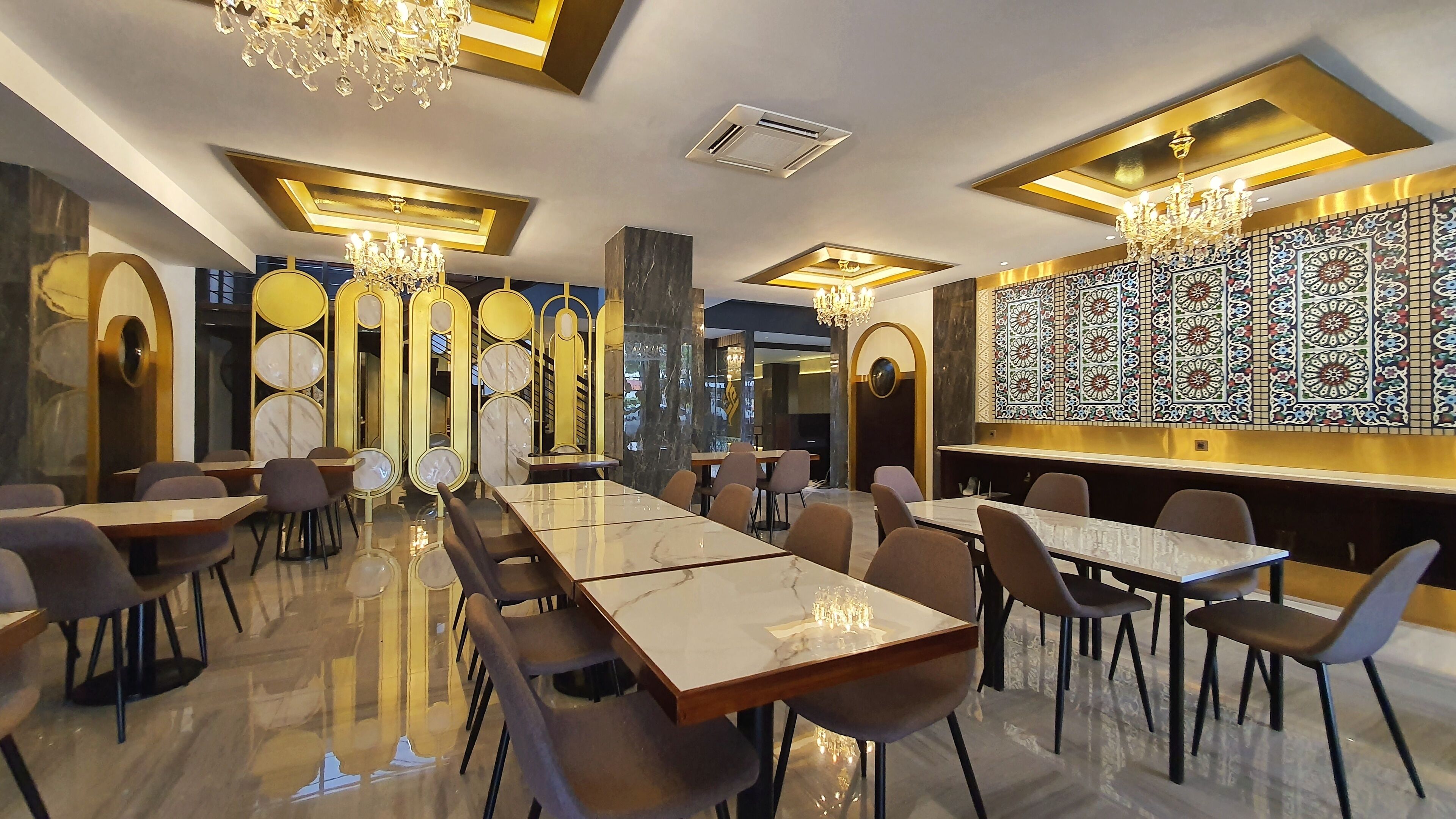 Un espace repas moderne avec des tables et des chaises en marbre, des lustres et des panneaux décoratifs muraux.