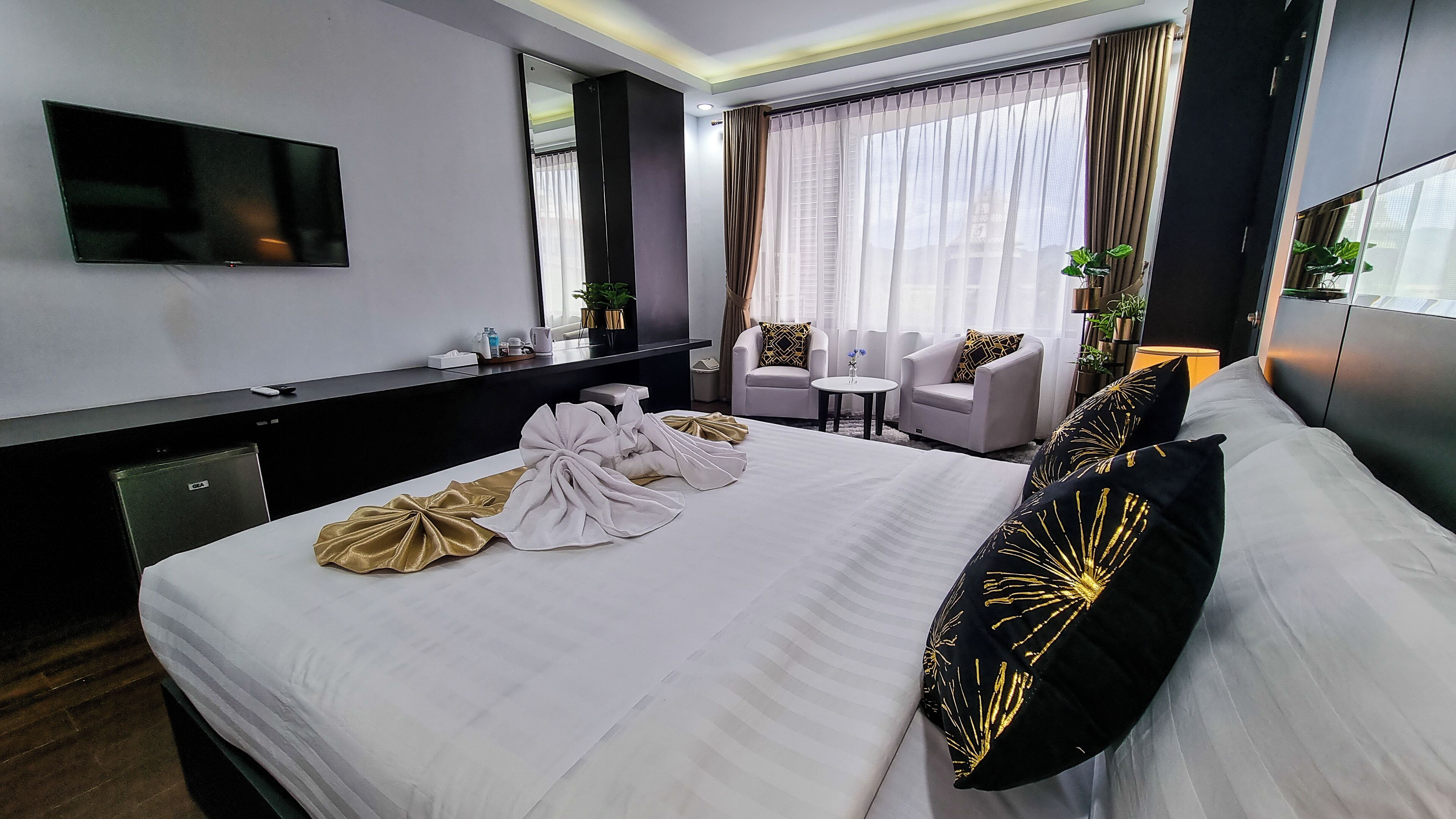 A hotel room with a large bed, a TV, a desk, and a seating area with chairs and a table.