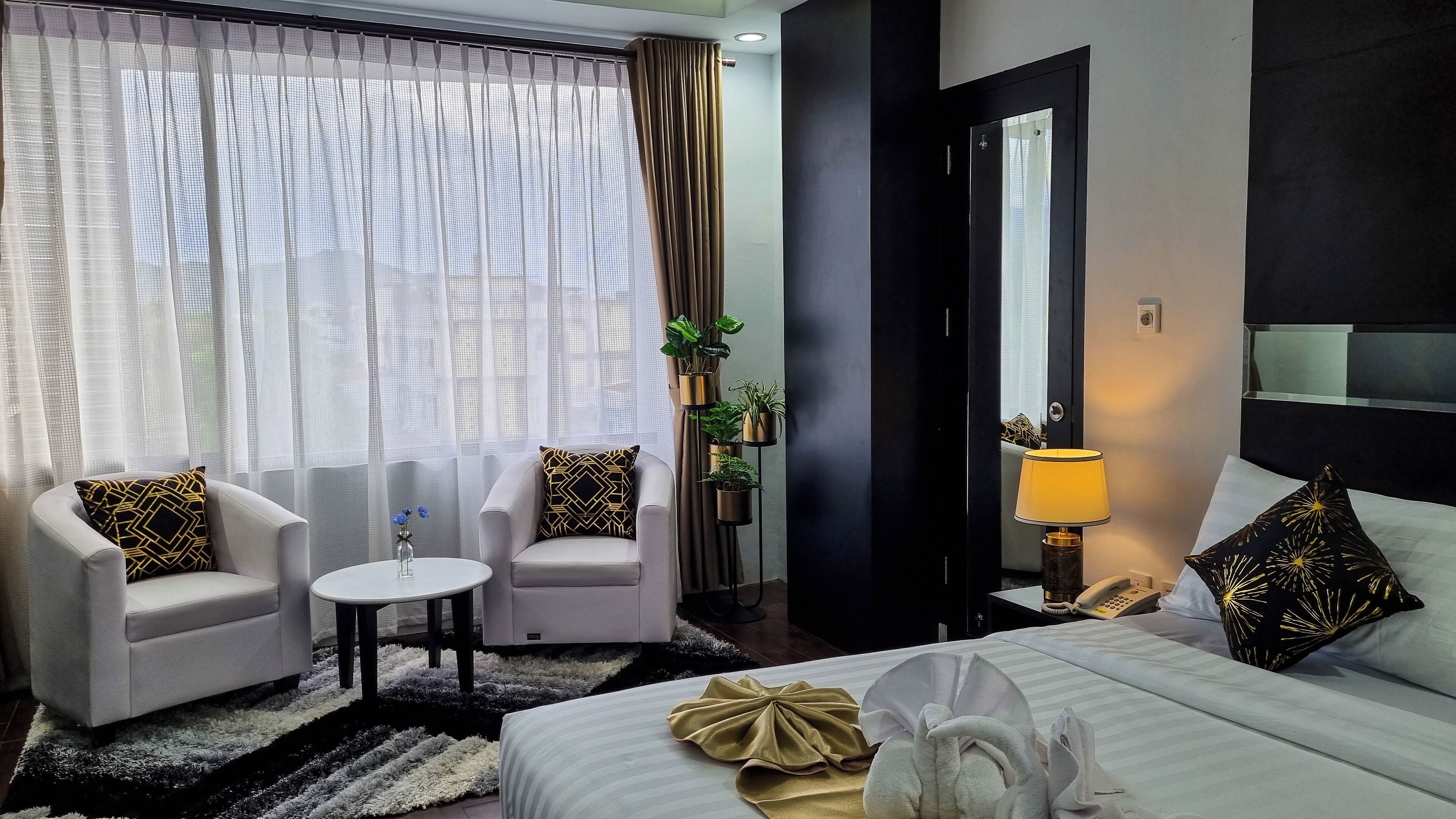 Habitación de hotel con una cama, dos sillones, una mesita, una lámpara y una planta en maceta.