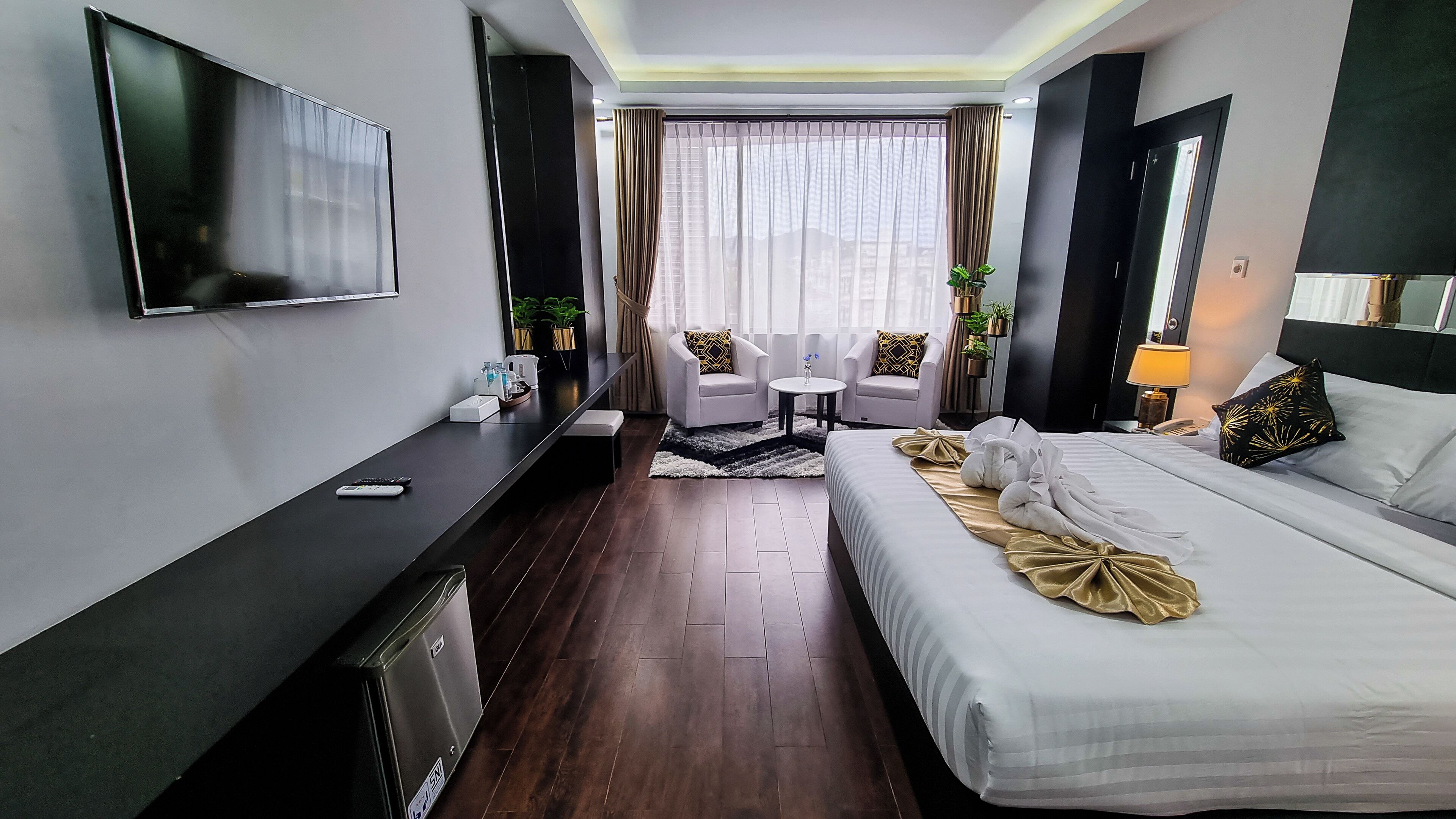 Quarto de hotel com cama, televisão, escrivaninha, cadeira e uma mesinha.