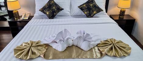 Una cama bien hecha con sábanas blancas, dos almohadas negras con un diseño de estrellas doradas y dos toallas con detalles dorados.
