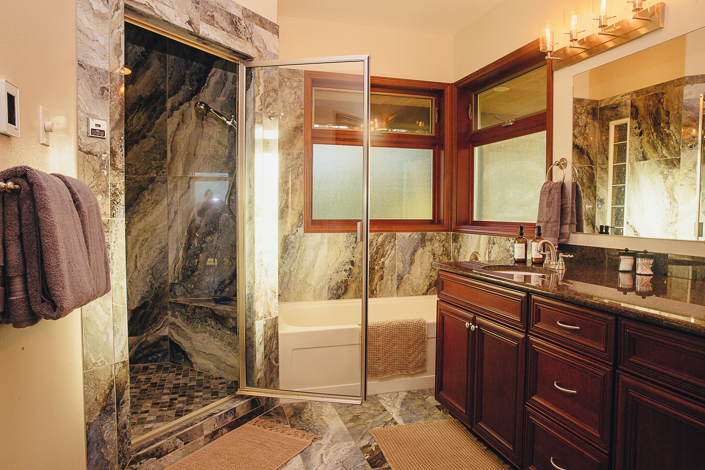 A bathroom with a glass-enclosed shower, a bathtub, and a vanity with a mirror.