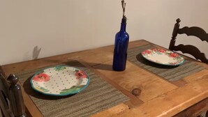 Une table de salle à manger en bois, avec deux assiettes à motifs floraux et un vase bleu.