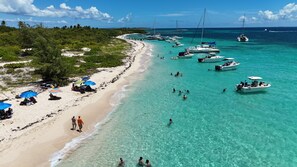 Una playa con agua turquesa cristalina, embarcaciones y gente nadando.