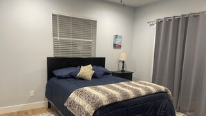 Un dormitorio con cama, mesita de noche, lámpara, ventana con persianas, alfombra y cortina.