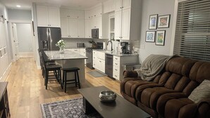 Una cocina moderna con armarios blancos, una isla central y un comedor con un sofá de cuero marrón.