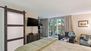 A hotel room with a bed, a sofa, a TV, and a sliding door leading to a balcony. - Salt Air Nook - Pool Access (Jekyll Island)