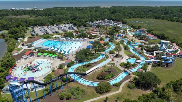 An aerial view of a water park with multiple slides and pools, surrounded by parking and greenery. - Salt Air Nook - Pool Access (Jekyll Island)