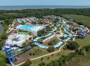 An aerial view of a water park with multiple slides and pools, surrounded by parking and greenery. - Salt Air Nook - Pool Access (Jekyll Island)
