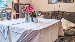 Une table à manger dressée avec une nappe blanche, deux vases ornés de fleurs roses, une bouteille de vin et un verre à vin.