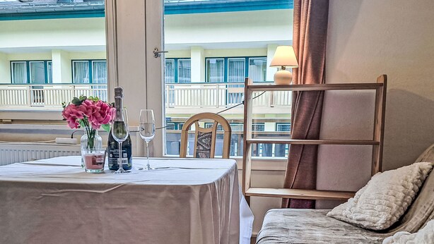 Une chambre d’hôtel avec un balcon, une table à manger ornée d’un vase de fleurs, des verres à vin et une chaise.