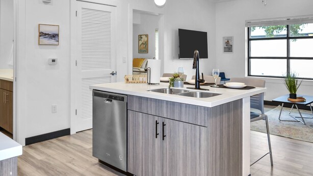 A modern kitchen with a dishwasher, a sink, and a dining area with a table and chairs. - King Suite & Twin Room | Condo at The Well Mouratoglou | Tennis & Pickleball (Zephyrhills)