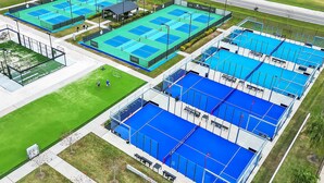 An aerial view of a sports complex with multiple tennis courts, seating areas, and a covered pavilion. - King Suite & Twin Room | Condo at The Well Mouratoglou | Tennis & Pickleball (Zephyrhills)