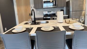 Une cuisine moderne avec une table à manger pour quatre personnes, comprenant un îlot central avec un saladier et des verres à vin.