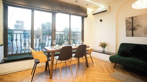 A dining area with a table set for four, large windows, a green sofa, and a wall-mounted air conditioner. - Apartment in the center of old Hanoi! (Hà Nội)