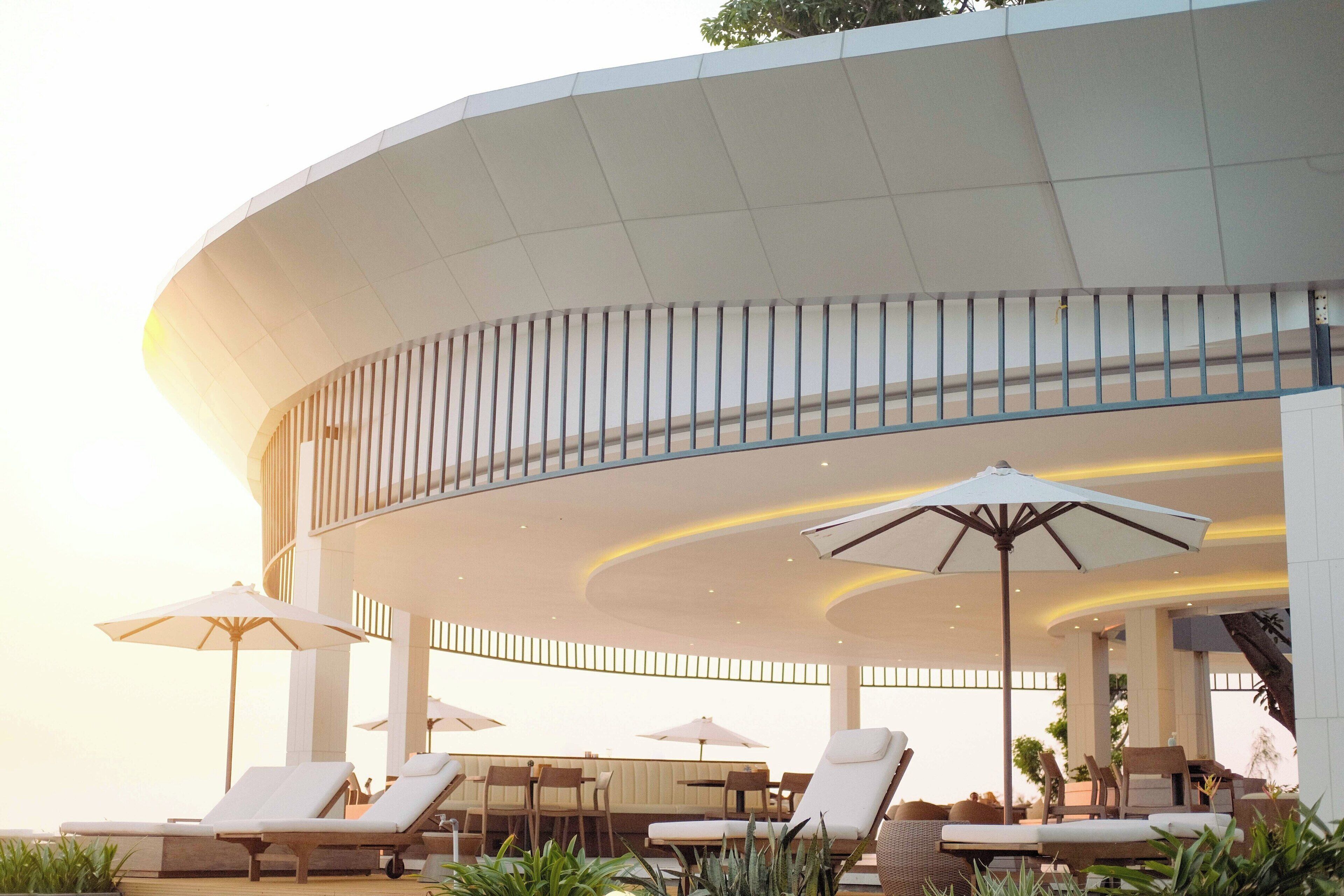 Zona relax esterna moderna con lettini e ombrelloni, caratterizzata da un design architettonico curvo e situata a bordo piscina.