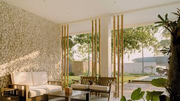A modern outdoor seating area with a stone wall, wooden furniture, and a view of a pool and greenery.