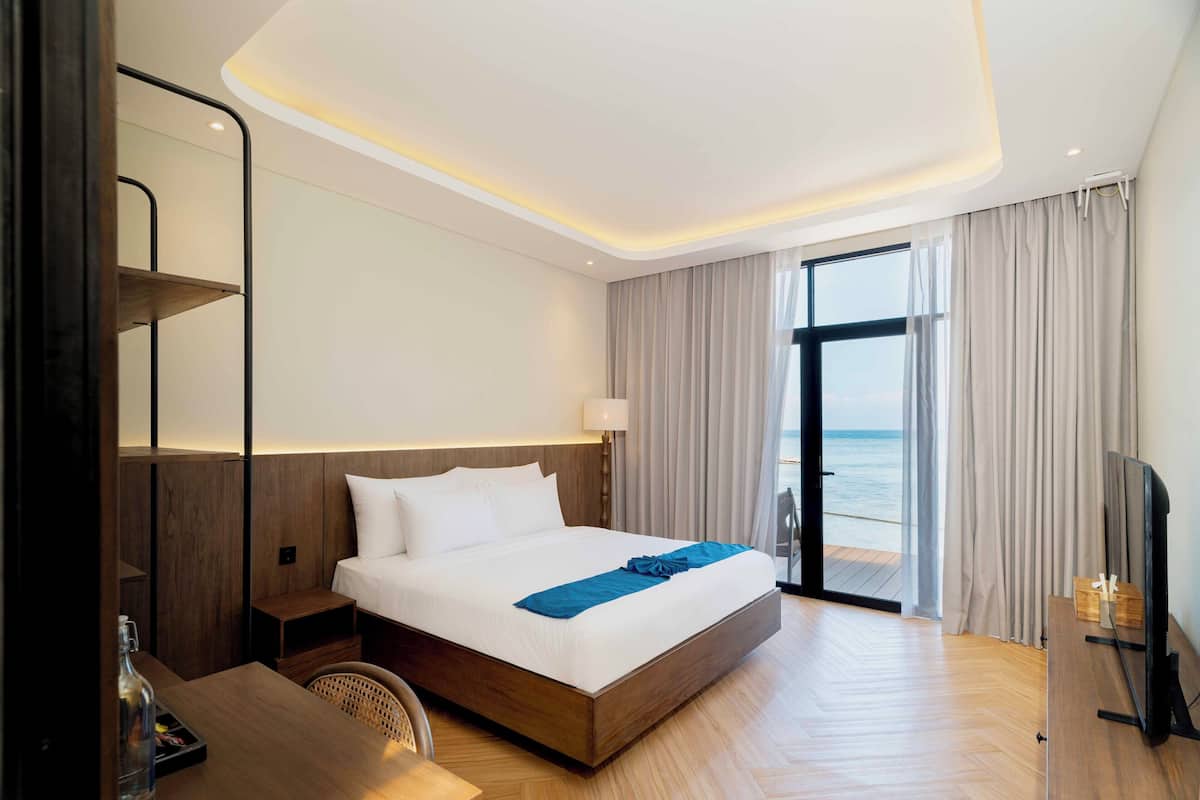 Una habitación de hotel moderna con una cama grande, una mesita de noche de madera, un escritorio, una silla y un televisor.
