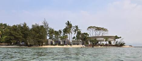 A beachfront property with multiple buildings, clear water, and palm trees.