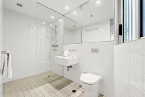 Un baño moderno con cabina de ducha de vidrio, un lavabo blanco y un inodoro.