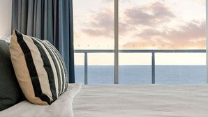 Een bed met een gestreept kussen en uitzicht op de oceaan door een balkonhek.