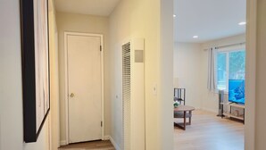 A hallway with a white door, a radiator, and a view of a living area with a TV and a window. - 261-6 Cozy 2-Bedroom Apartment near Downtown Mountain View (Mountain View)
